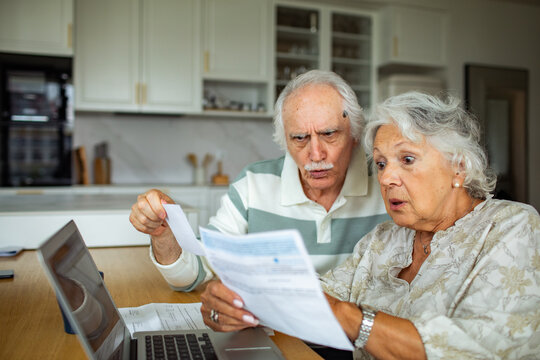 Shocked senior couple reviewing bills at home kitchen
