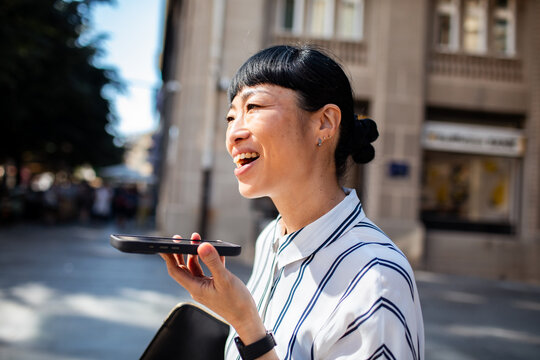 Smiling woman using voice assistant on smartphone outdoors in city