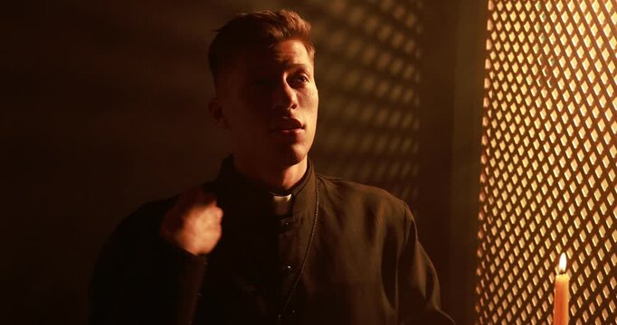 Priest praying near wooden window in confessional booth. Camera moving forward and backwards