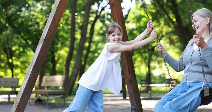 Smiling granddaughter pushing her grandmother on swing in park