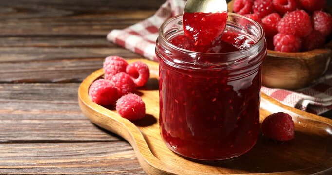 Stirring sweet raspberry jam in jar on wooden table, closeup. Space for text