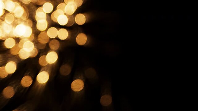 Abstract golden bokeh light particles shimmering in the corner on a solid black background.