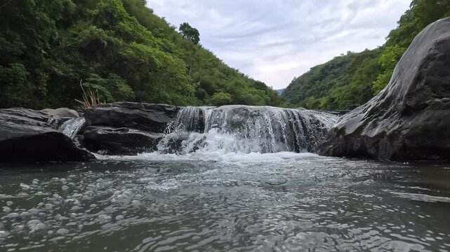 Low angle shot of a small waterfall cascading into a bubbling mountain river, 4K b-roll