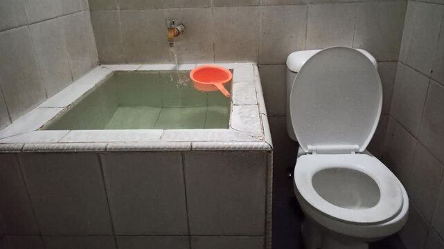 A traditional Indonesian-style bathroom featuring a white ceramic bathtub, modern sitting toilet, and functional interior design that blends comfort with local architectural elements.