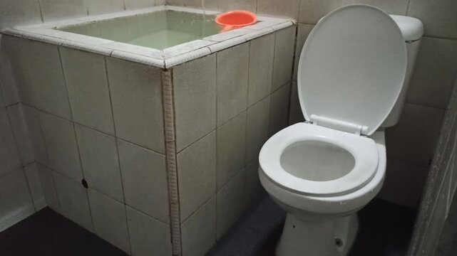 A traditional Indonesian-style bathroom featuring a white ceramic bathtub, modern sitting toilet, and functional interior design that blends comfort with local architectural elements.