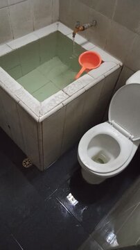 A traditional Indonesian-style bathroom featuring a white ceramic bathtub, modern sitting toilet, and functional interior design that blends comfort with local architectural elements.