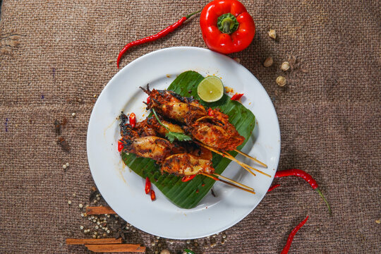 Grilled Squid Skewers with Padang Spices on Banana Leaf

Description
Skewered grilled squid coated in a rich reddish brown Padang style spice glaze rests on a fresh banana leaf atop a white plate, gar