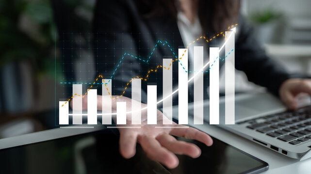 A business professional engages in extensive financial analysis using virtual graphs, showcasing growth trends and strategic insights in a modern office environment. Impute