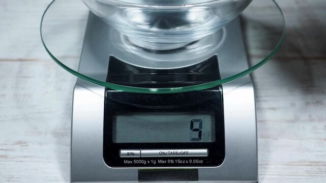 Measuring ingredients with an empty glass bowl on a digital kitchen scale for baking.