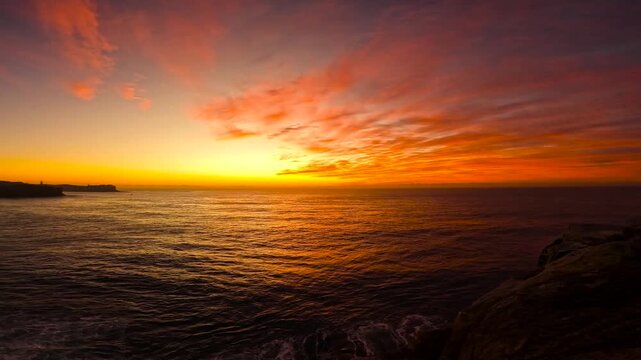 Timelapse video of glowing red sunrise above the ocean with vibrant reflections on the water at Bronte Beach, Sydney, Australia.