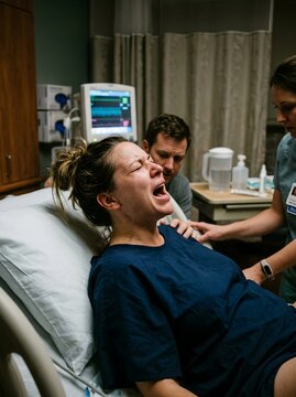 Woman in Active Labor Screaming During Contraction with Husband and Nurse Supporting in Hospital Delivery Room