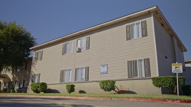 Daytime shot of a two-story multifamily housing building with siding exterior, shuttered windows, and a security sign on the lawn.