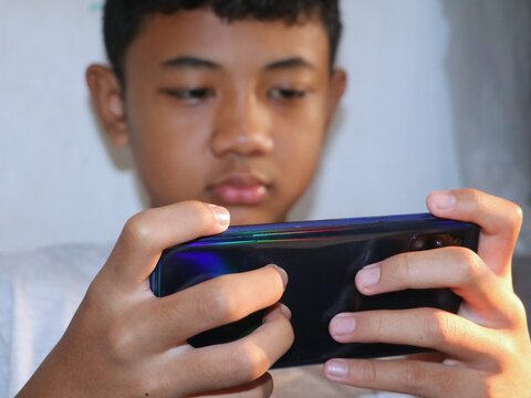 A close-up view focusing on an Asian boy's hands holding a smartphone in a landscape position, focused intents on screen-time activity or gaming