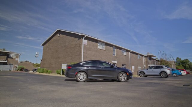 Sunny daytime view of a brick multifamily housing complex with vehicles in the parking lot.