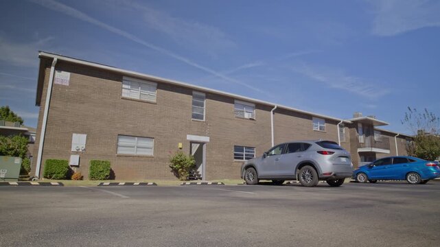 Sunny daytime view of a multifamily housing building with a parking lot and parked vehicles.