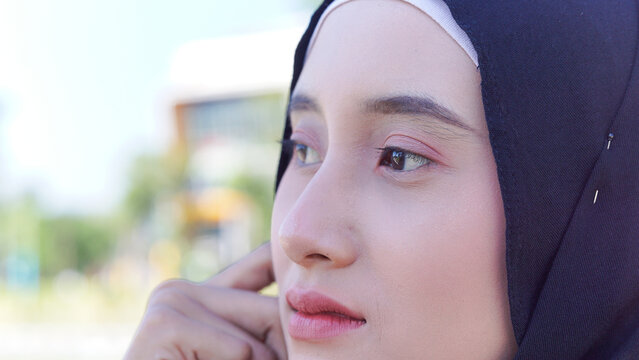 Detailed close-up of a young woman's lower face and hand adjusting her black hijab