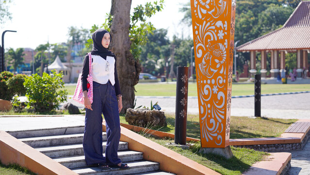 Smiling Young Asian Muslim Woman in Black Hijab and Vest Standing Outdoors in Park