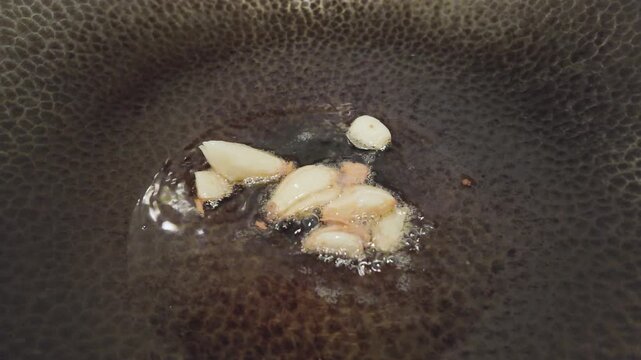Garlic Cloves Frying in Hot Oil Turning Golden Brown in Iron Pan