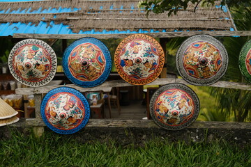 Traditional woven Balinese conical hats painted with Balinese motifs hanging on a roadside warung fence © Юрий Несмашный