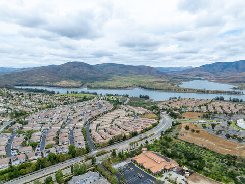 An aerial view of a large housing community near Otay Lakes in Chula Vista featuring dense suburban single-family blocks, winding green parkways, and close proximity to the Lower Otay Lake reservoir