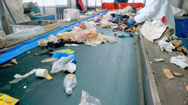 Workers sorting garbage on conveyor belt at recycling plant for waste management and disposal.
