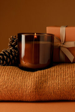 Candle, cones and box on sweater on orange background