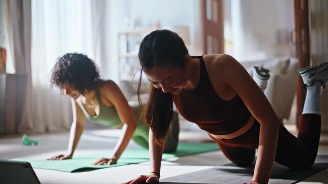 Two women doing pushups yoga mats home. Fitness training together with tablet.