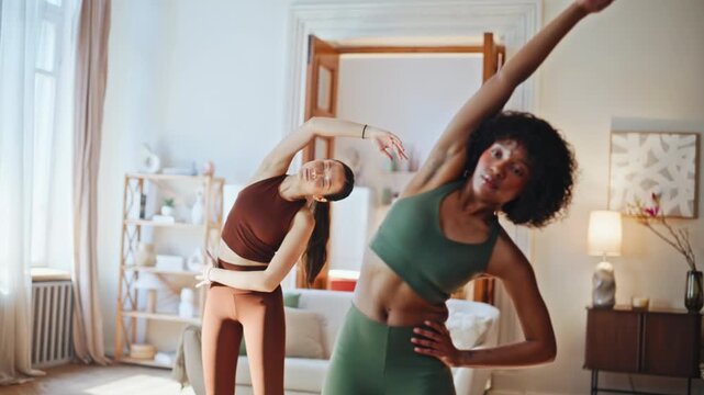 Diverse women side stretches home living room. Fitness workout morning routine.