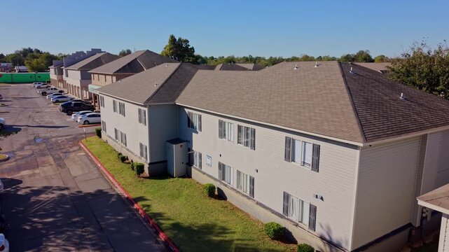 Daytime aerial view of a multifamily housing complex showing rows of residential units and an adjacent parking lot.