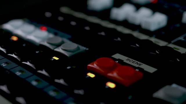 A close-up of a person's hand operating controls on a dark professional studio mixing console with blue accent lighting.