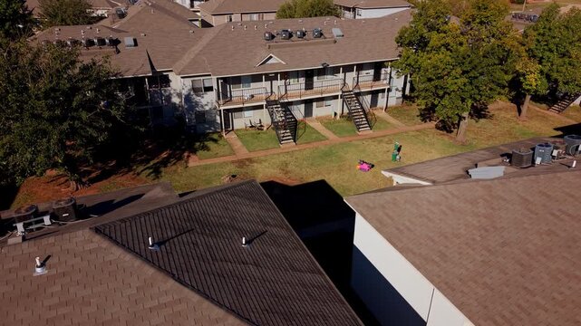 Daytime aerial view of a multifamily housing complex with rows of units, exterior stairs, and shaded pathways.