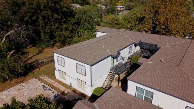 Daytime aerial view of a residential building with surrounding trees, yard, and open spaces.