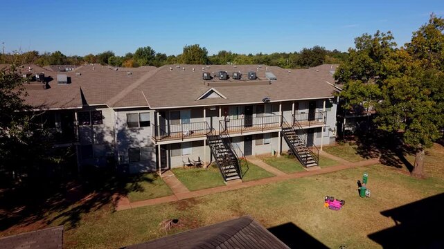 Daytime shot of a row of apartment units with exterior staircases, balconies, and a grassy yard with a child's toy car.
