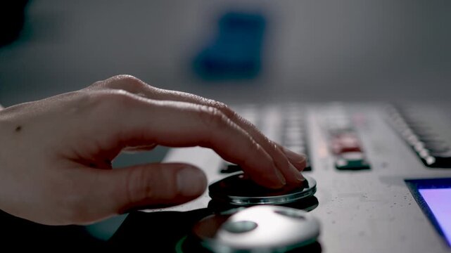 A close-up of a person's hand resting on a dial or knob of a professional broadcast studio mixing console.