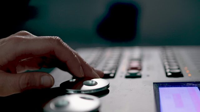 A close-up of a person's hand operating controls on a dark professional studio mixing console with blue accent lighting.