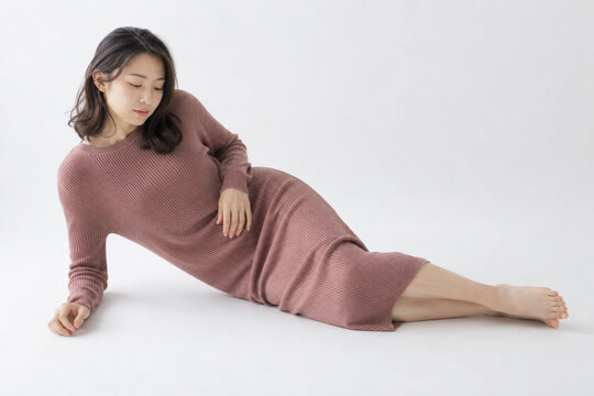 白いスタジオで横たわるローズ色ニットドレスの女性