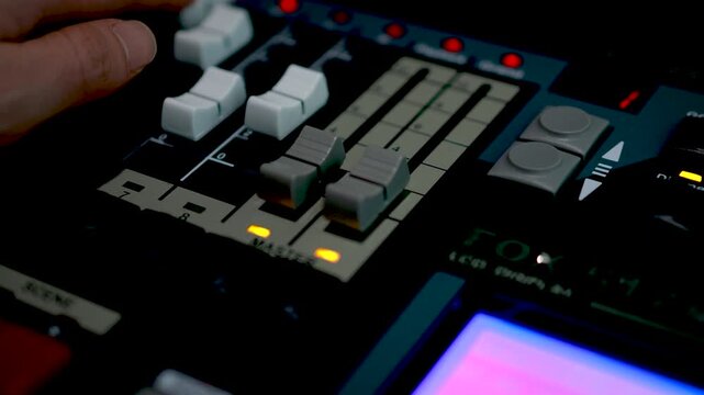 A close-up of faders and colorful indicator lights on a professional studio mixing board in a broadcast or recording facility.