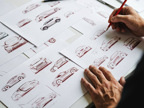 Automotive designer sketching modern car concept prototypes on paper in a creative design studio top down workspace view