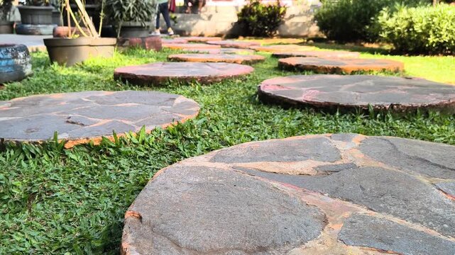 Low angle view of a person walking on textured circular stepping stones across a bright green grass lawn in a peaceful outdoor garden.