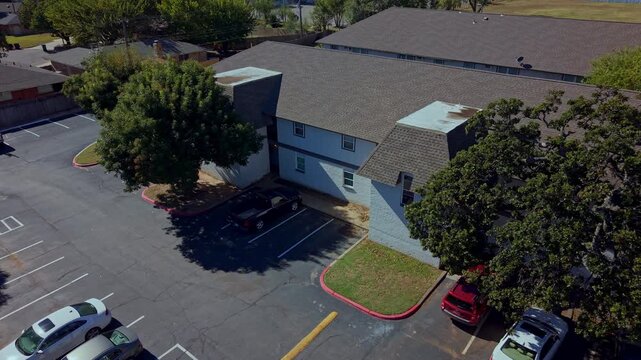 Daytime aerial view of a residential building with a surrounding parking lot and tree coverage.