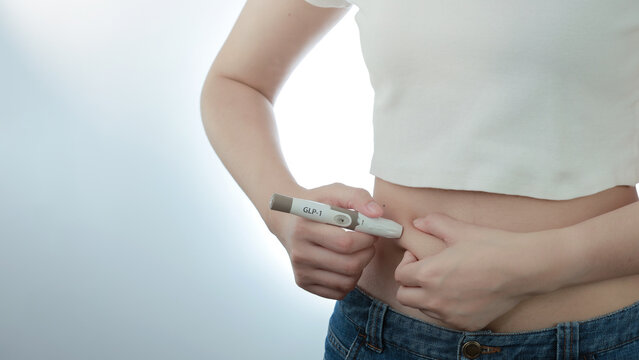 Focused woman uses modern medical injection pen on abdomen for weight loss treatment, managing health with careful therapy