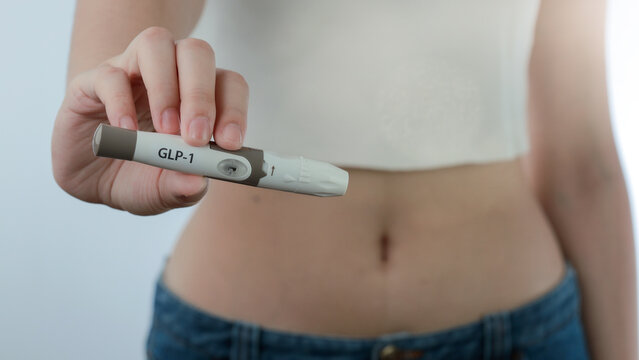 Confident young woman holding modern medical weight loss injection pen close to her slim abdomen with hopeful and determined expression