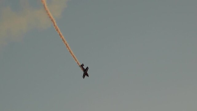 Airplane performing aerobatic maneuvers with smoke trail against sky