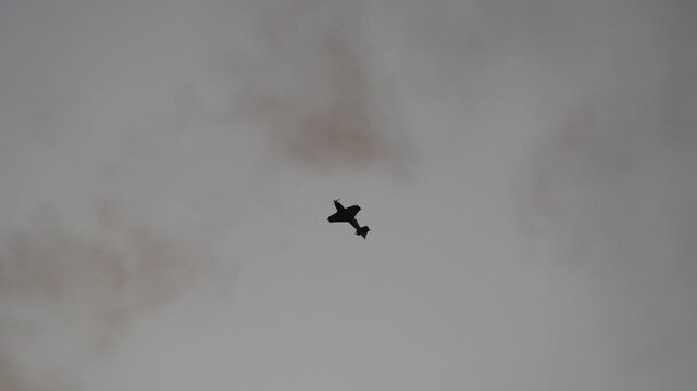 Airplane performing aerobatic maneuvers with smoke trail against sky