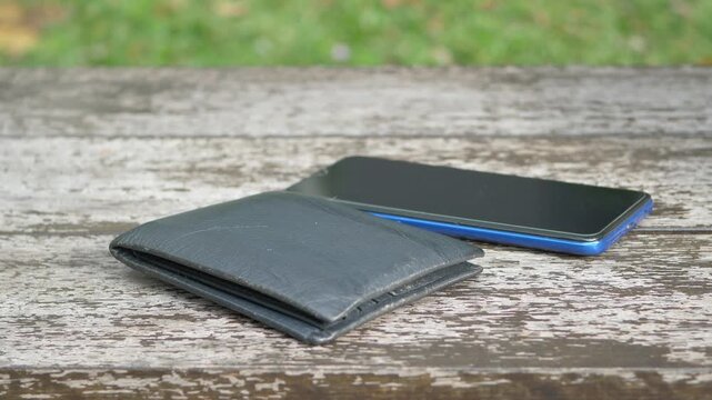 Smartphone and wallet sitting on wooden outdoor table with grass background during daylight