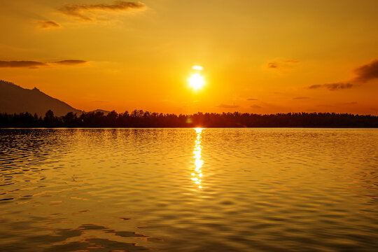 Golden Sunsets over Borovoe lake in Kazakhstan, path of light reflects on calm rippling water, orange and gold colored sky glows.  Burabay National Nature Park Travel destination. Serene and peaceful