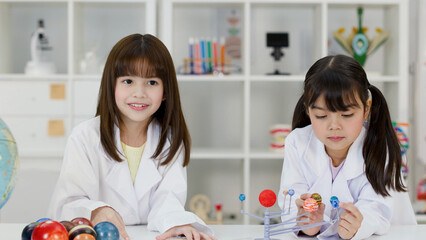 Two Elementary School Girls in Lab Coats Studying Solar System Model © blueringmedia