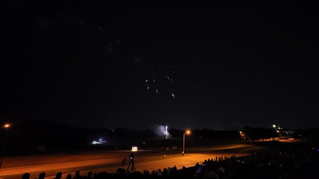 Fireworks exploding over a stadium field at night with spectators