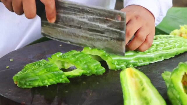 Chef chopping organic bitter gourd on wooden board surrounded by fresh harvest 4K