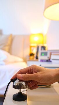 Close up of a person hand pressing a hotel service call bell on a bedside table in a bedroom